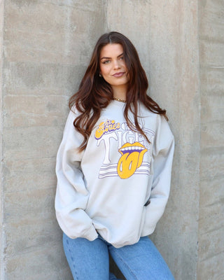Woman wearing a white sweatshirt with graphic design against a concrete wall
