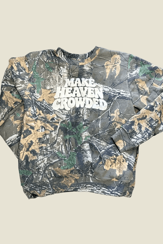 A long-sleeve crewneck sweatshirt featuring a distressed camouflage pattern in green, brown, and gray, with the phrase 'MAKE HEAVEN CROWDED' printed in bold white letters across the chest.