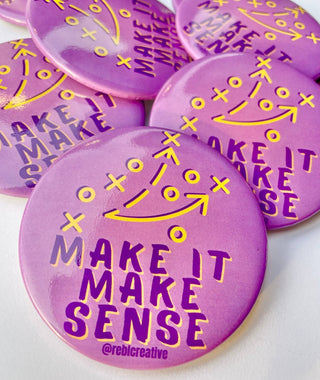 A close-up of several round purple pins or badges with yellow football play symbols and the phrase “MAKE IT MAKE SENSE” printed on them. One pin at the bottom also shows the handle “@rebicreative.