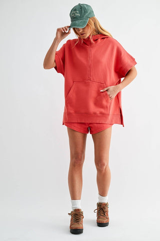 Person wearing a red hoodie and shorts with a green cap on a white background