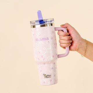 Hand holding a pink tumbler with 'mama' and floral design on a beige background