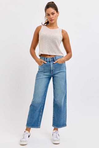 Woman wearing a white tank top and blue jeans on a white background