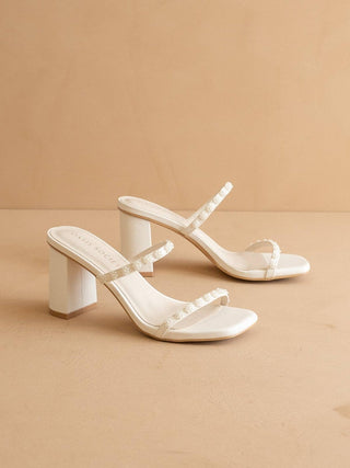 Pair of white high-heeled sandals on a beige background