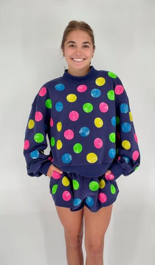 Person wearing a navy sweatshirt and shorts with colorful polka dot pattern on a white background