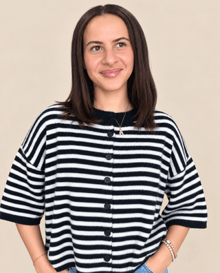 A woman with shoulder-length brown hair wearing a black and white horizontally striped knit cardigan with a black collar and front buttons, photographed against a plain beige studio background.