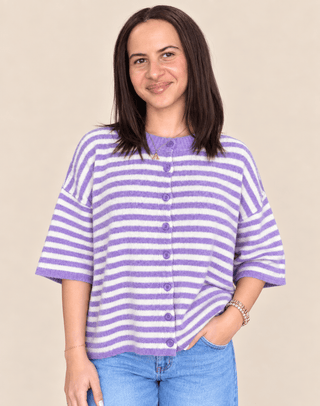 A woman wearing a lavender and white striped knit cardigan with a button-down front, paired with blue jeans, against a solid beige background.