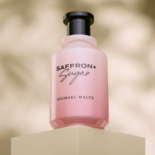 Pink perfume bottle labeled 'Saffron + Sugar' by Michael Malul on a beige background