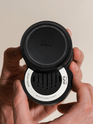 Black Pura candle diffuser held by hands against a beige background