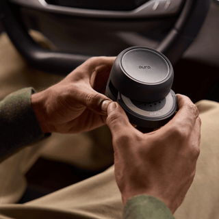 A close-up of a person's hands holding a dark gray circular Euro Air personal air purifier inside a car interior.