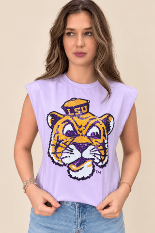 A woman wearing a lavender sleeveless crop top with a large LSU Tigers mascot graphic on the front, paired with light blue jeans, set against a solid beige background.