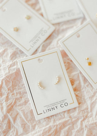 Pearl earrings on LINNY CO branded cards with a soft pink background