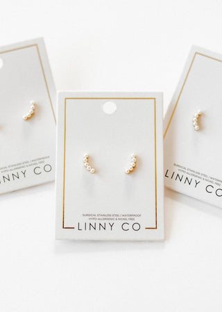 Pair of pearl earrings on LINNY CO branded card with additional cards in the background.