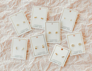 Gold earrings on LINNY CO cards against a pink marble background