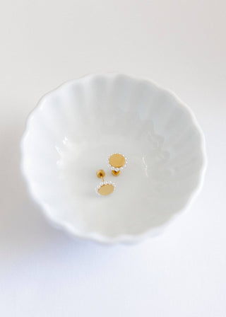 Pair of gold and pearl stud earrings on a white dish.