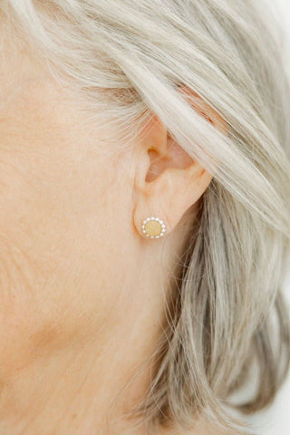 Close-up of an ear wearing a small gold earring with a clear gemstone.