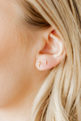 Close-up of an ear wearing gold stud earrings with a blurred background