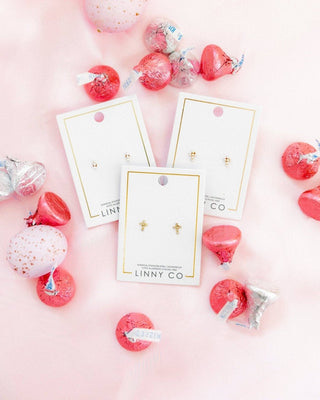 LINNY CO earrings on display with decorative pink and red items on a pink background