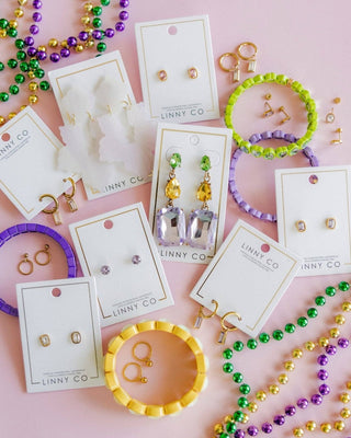 Jewelry set including earrings and bracelets on LINNY CO cards with colorful beads on a pink background.