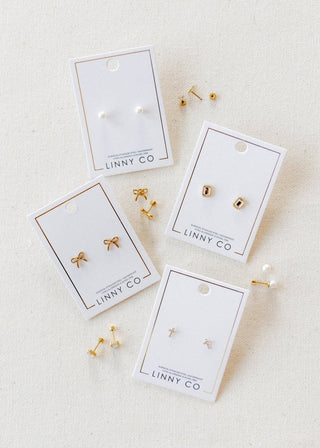 Gold earrings on LINNY CO branded cards on a beige fabric background