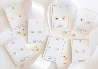 Gold earrings on LINNY CO display cards against a white background