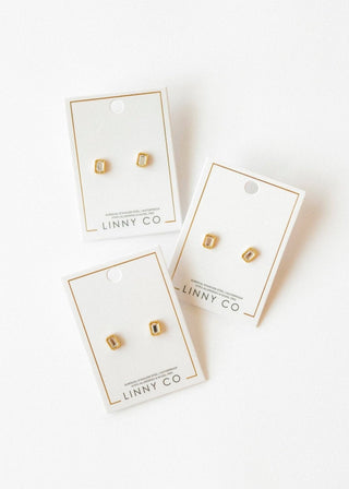 Three pairs of gold square earrings on LINNY CO cards against a white background