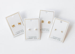 Four pairs of earrings on LINNY CO branded cards against a white background