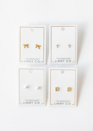 Four pairs of gold earrings on LINNY CO cards against a white background