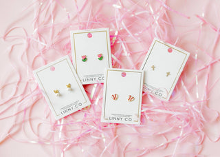 Set of earrings on LINNY CO cards with pink ribbons in the background
