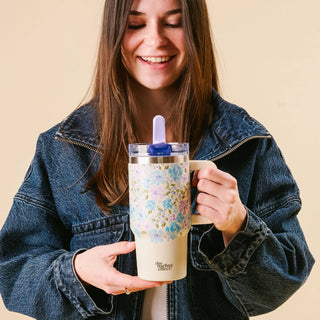 Woman holding a floral-patterned tumbler with a blue straw lid against a beige background