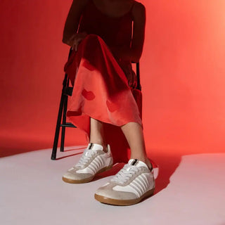 Person wearing white sneakers with brown soles sitting on a stool against a red background