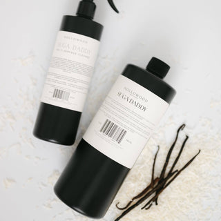 Two black bottles labeled 'Sugardaddy' on a textured white surface with vanilla beans.