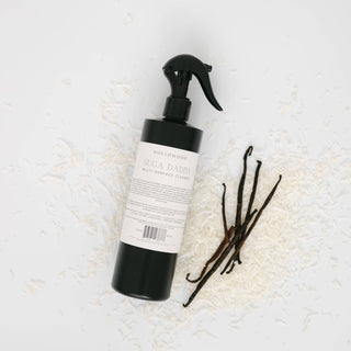 A black spray bottle labeled 'HOLLOWOOD SUGA DADDY MULTI-HEMPF CLERSE' with vanilla beans and white coconut flakes on a white background.