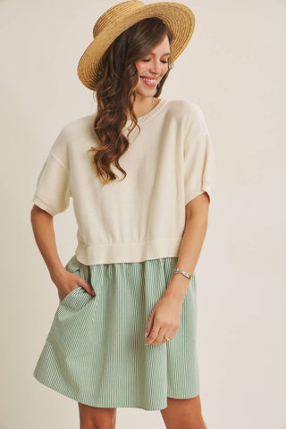 A woman wearing a cream short-sleeve knit top and a light green and white vertically striped skirt, styled with a straw hat against a plain beige background.