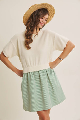 A woman wearing a cream short-sleeve knit top and a light green vertically striped pleated mini skirt, styled with a straw hat against a plain beige background.