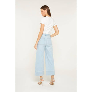 Woman wearing light blue pants and a white top on a plain background