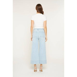 Woman wearing light blue wide-leg jeans and a white top on a plain background