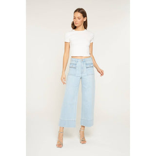Woman wearing a white crop top and light blue jeans on a plain background