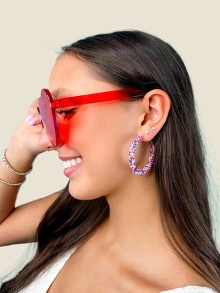 Woman wearing red sunglasses and colorful hoop earrings against a blue background