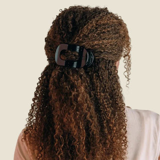 Person with long, curly hair wearing a black hair clip on a white background