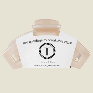 A translucent beige hair clip with a white paper label that reads 'say goodbye to breakable clips! TELETIES the hair clip, reinvented' on a light beige background.