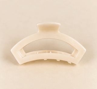 A cream-colored semi-rigid hair claw clip on a solid beige background.