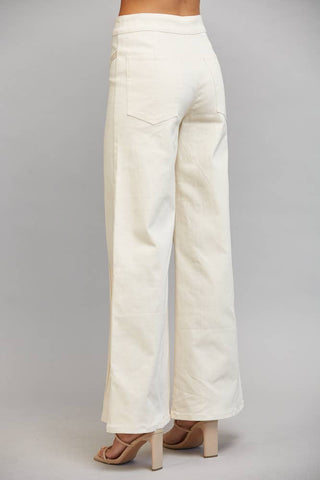 A person shown from the back wearing off-white wide-leg pants and beige heeled sandals against a light gray studio background.
