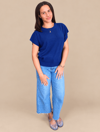 A woman modeling a royal blue short-sleeve t-shirt and light wash wide-leg jeans against a solid beige studio background.