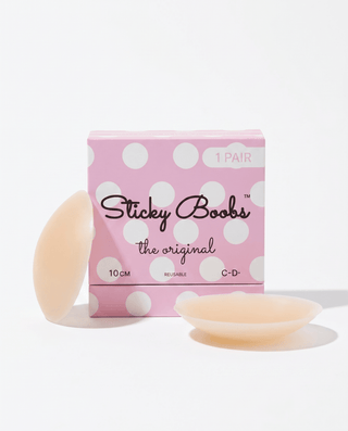 A pink polka-dot box labeled 'Sticky Boobs the original' with two pale peach silicone breast-shaped stickers placed in front on a clean white background.