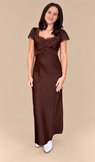Model wearing a full length Chocolate brown satin dress with lace trim on a tan background

