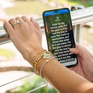 Person holding a phone with a verse displayed, wearing multiple bracelets.
