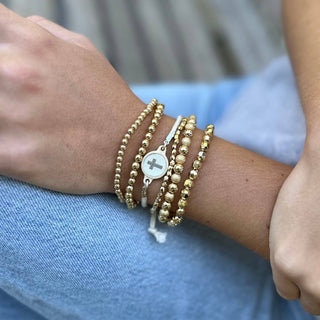 Close-up of a wrist wearing gold beaded bracelets with a blurred background