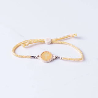 Yellow bracelet with a central circular charm on a light gray background