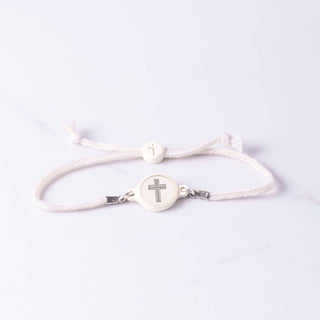 White bracelet with a cross charm on a light gray background