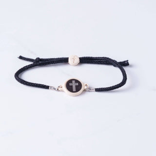 Black braided bracelet with a silver cross charm on a light gray background